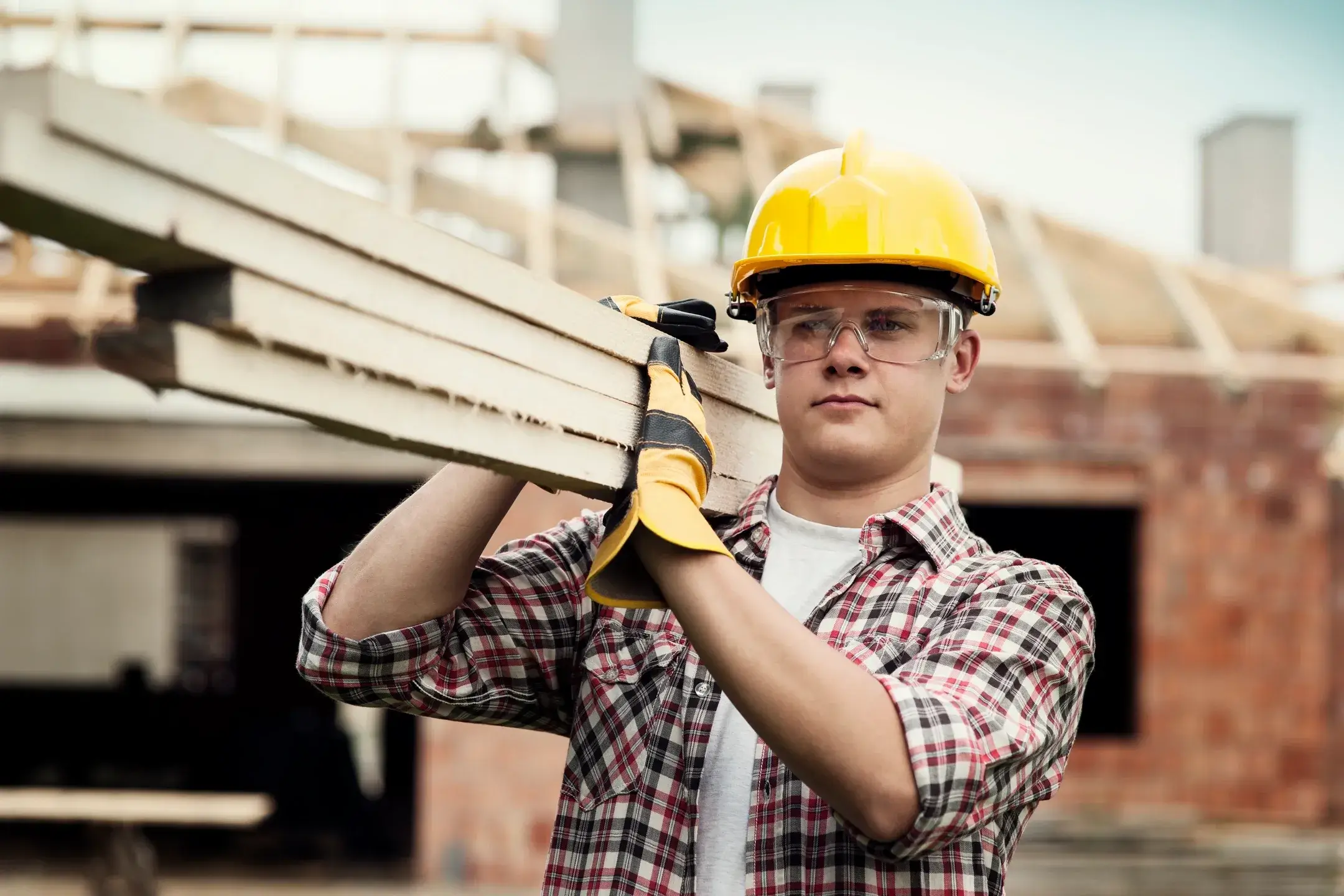 Construction worker carrying timber on a building site.