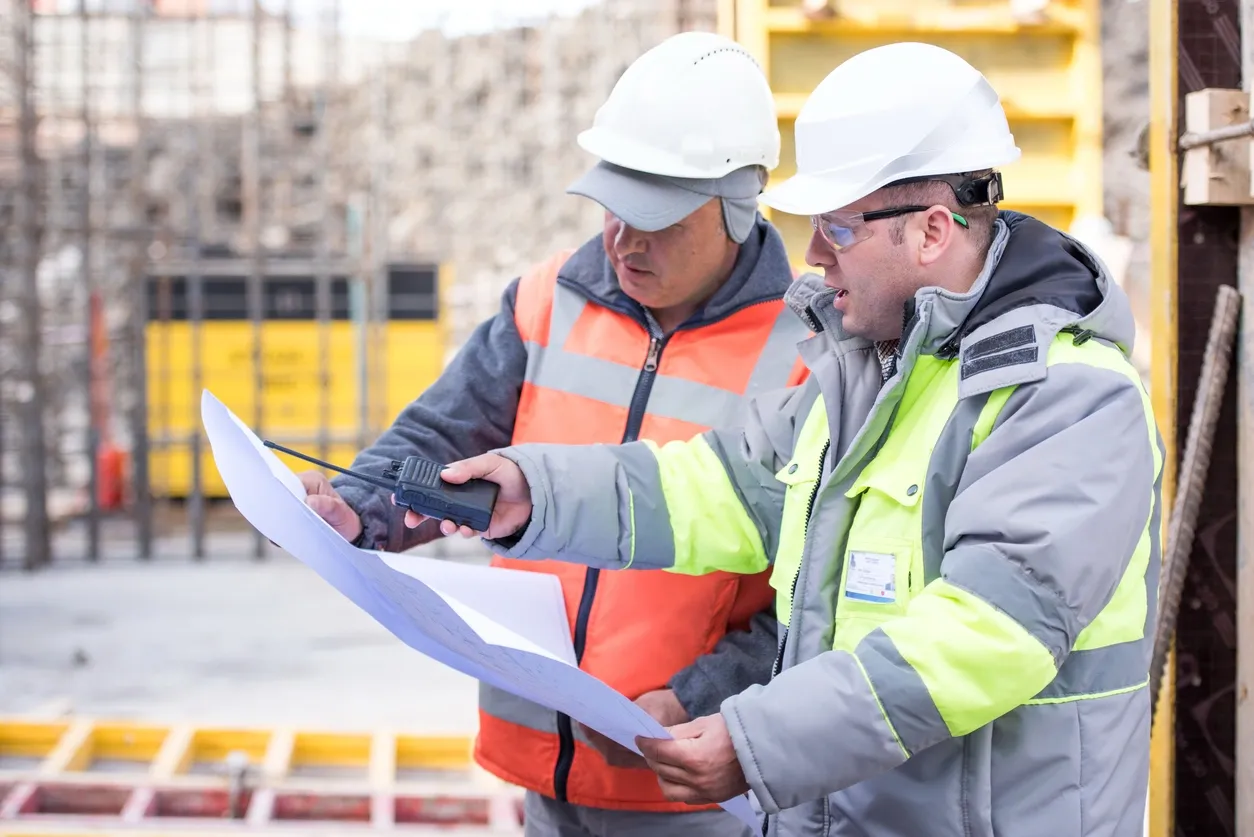 Two construction workers reviewing blueprints on-site.