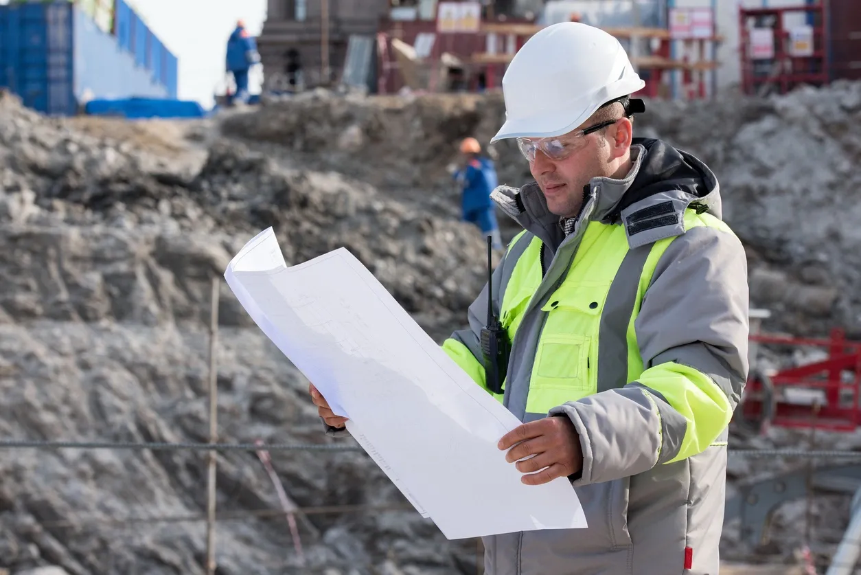 Engineer reviewing construction plans on site wearing safety gear.